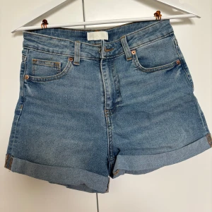 Blå jeansshorts från H&M - Säljer ett par snygga blå jeansshorts från H&M i storlek 38/M. Shortsen har en liten fläck längre ner på shortsen och vid fickan som inte går bort i tvätten, men inget man lägger märke till.                                                     Midjemått rakt över: 34,5cm                               Innerbensmått: 8cm                                                 Hela benet: 33cm