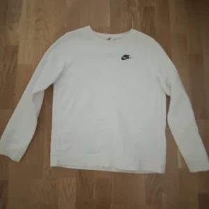 Vit Nike sweatshirt - Säljer en stilren vit långärmad tröja från Nike med deras klassiska logga på bröstet. Perfekt för en avslappnad och sportig look. Passar bra till både jeans och träningsbyxor. Storlek: 158-170