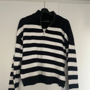 Svartvit randig stickad tröja halvzip - Säljer en stilren svartvit randig stickad tröja med dragkedja vid halsen. Tröjan har långa ärmar och är perfekt för kyligare dagar. Den ribbade strukturen ger en extra touch av stil. Passar bra till både jeans och kjol.