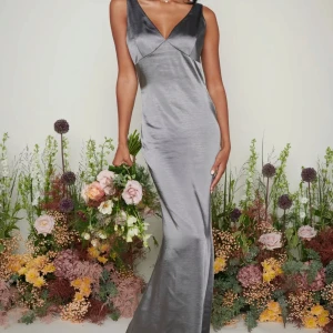 Grå långklänning i satin - Elegant grå långklänning i satin med v-ringning och ärmlös design. Perfekt som balklänning, för egna bilder - skriv privat💕💕 Aldrig använd från Pretty Lavish, nypris ca 1500 ikl frakt och tull