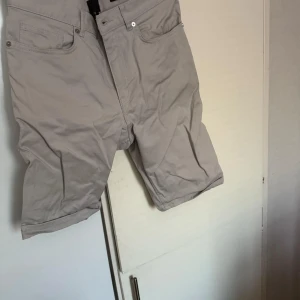 Beige slim fit shorts - Säljer ett par stilrena grå shorts i slim fit. De har en klassisk design med fem fickor och knappstängning. Perfekta för en avslappnad look.
