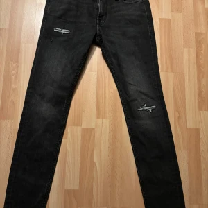 Svarta jeans med slitningar - Snygga svarta jeans med slitningar på låren. De har en tight passform och är perfekta för en trendig look. Midjan är midwaist och storleken är w29. Perfekta för att ge din outfit en edgy touch. Använda 1 gång.