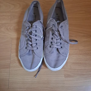 Beige sneakers med snörning - Säljer ett par stilrena beige sneakers med snörning. Skorna har en vit sula och är perfekta för en avslappnad look. De är bekväma och passar till många olika outfits.
