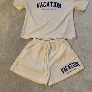 Vit t-shirt med tryck - Säljer en vit t-shirt med blått tryck 'VACATION' och texten 'EVERY DAY IS A NEW DAY' under. T-shirten har korta ärmar och en avslappnad passform. Perfekt för en ledig dag eller semester.