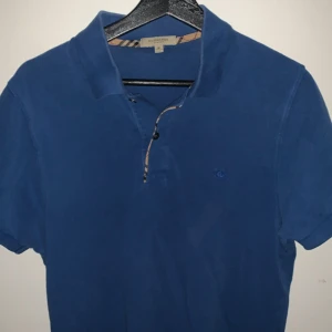 Blå pikétröja från Burberry - Säljer en blå burberry piké tröja, perfekt för sommaren och en färg som lätt går att stylea. Nästan helt ny! Hör av er vid intressen