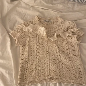 Beige stickad topp från Zara  - Säljer en söt beige stickad topp från Zara med korta ärmar och volangdetaljer vid halsen. Perfekt för en stilren stil eller till sommaren