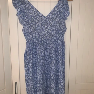 Blå blommig klänning - Luftig sommarklänning med blåvitt blommönster. Den knyts baktill med band, så den passar flera olika storlekar. Saknar lapp men kommer förmodligen från HM eller liknande