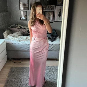 Rosa satinlångklänning från OhHelloClothing - Säljer en söt rosa långklänning i satin från Oh Hello Clothing som är helt utsåld! Klänningen har en one-shoulder design och en smickrande omlott-detalj i midjan. Perfekt för speciella tillfällen som bal osv. Klänningen är aldrig använd och har alla lappar kvar!
