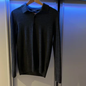 Mörkgrå långärmad pikétröja - Säljer en stilren mörkgrå långärmad pikétröja med klassisk krage och knappar framtill. Perfekt för en avslappnad men ändå uppklädd look. Passar bra till både jeans och chinos.