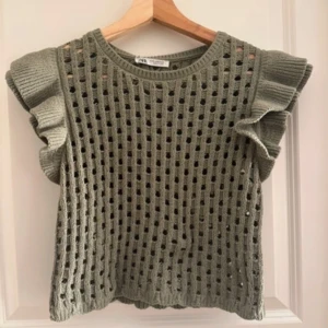 Stickad grön topp med volangärm Zara - Superfin stickad topp från Zara i en mjuk grön nyans. Toppen har ett hålmönster över hela och coola volangärmar som ger extra edge. Rund halsringning och ribbade kanter. Perfekt för dig som vill ha något unikt och trendigt i garderoben. Helt oanvänd med prislapp kvar.