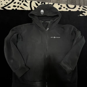 Svart hoodie från Sail Racing - Svart hoodie från Sail Racing med dragkedja och huva. Framtill finns logga på bröstet och en vit detalj på huvan. Tröjan har två stora fickor och är tillverkad i mjukt material, perfekt för kyliga dagar. Passar bra till S 