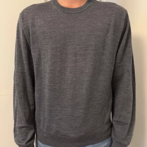 Mörkgrå stickad tröja från Sandö - Säljer en stilren mörkgrå stickad tröja från Sandö i storlek L. Tröjan har rund halsringning, ribbade muddar och är långärmad. Perfekt för lager-på-lager och passar till jeans eller chinos. Enkel och clean look som funkar till det mesta.
