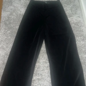 Svarta vida byxor i sammet - Säljer ett par svarta byxor med breda ben och hög midja. Byxorna är gjorda i mjuk sammet som ger en lyxig känsla och snyggt fall. Perfekta för dig som gillar en trendig och avslappnad stil.