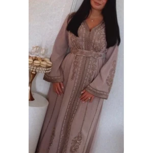 Kaftan - Taupe-färgad kaftan i storlek S, använd endast en gång. Passar XS-M då bältet kan knytas åt efter behov. Elegant och handsydd med vackra detaljer, perfekt till bröllop, fest eller högtider. Bälte ingår.