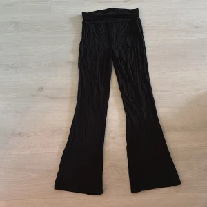 Svarta vida byxor i mjukt tyg - Svarta byxor med hög midja och vida ben, tillverkade i ett mjukt och stretchigt material. Perfekta för en chill och avslappnad stil. Passar dig som gillar bekväma och trendiga plagg med lite extra sväng i benen.