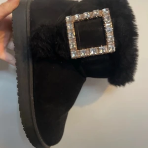 Svarta boots/uggs med päls och strass - Mysiga svarta boots med fluffig päls och en stor fyrkantig spänne. Tjock sula och mjukt material för maximal komfort. Skicka prisförslag