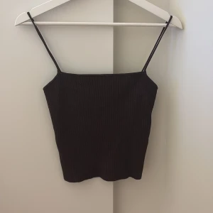 Svart ribbad linnetopp från H&M - Aldrig använd!! Den ser svart ut men den är mörkbrun. En svart ribbad linnetopp från H&M med smala axelband och rak halsringning. Toppen är figurnära och har en enkel, stilren look som passar perfekt till jeans eller kjol. Materialet är stretchigt och bekvämt, vilket gör den lätt att bära hela dagen.