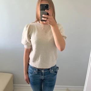 Beige stickad tröja med puffärm - Säljer en beige stickad tröja med korta puffärmar och rund hals. Tröjan har ribbade muddar vid ärmslut och nederkant, vilket ger en snygg och modern look. Perfekt för dig som gillar en stilren men ändå trendig vibe.