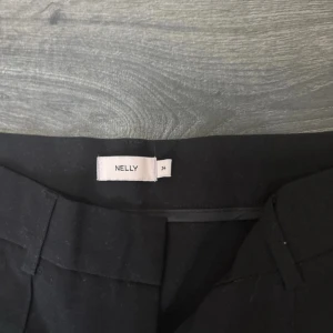 Svarta bootcut byxor från Nelly - Snygga svarta bootcut byxor från Nelly i klassisk modell med pressveck och hällor för bälte. Byxorna har en figurnära passform upptill och vida ben nertill, vilket ger en riktigt clean och trendig look. Perfekta att styla med sneakers eller klackar. Pris kan diskuteras 