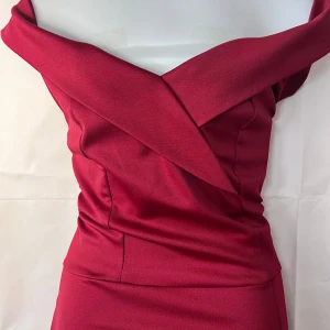 Vinröd axelbandslös långklänning med slits  - Säljer en elegant vinröd långklänning med omlott-detalj upptill och en snygg slits framtill. Klänningen är axelbandslös och har en figurnära passform som framhäver siluetten. Perfekt för festliga tillfällen!