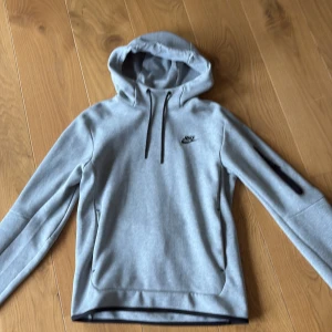 Grå hoodie från Nike  - Nästan helt oanvänd ljusgrå hoodie från Nike. Tröjan har huva med svarta snören, svart Nike-logga på bröstet och en ficka med dragkedja på ärmen. Hoodien är varm och bra till vintern.