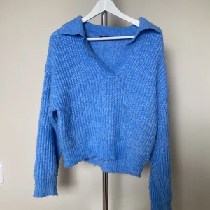Blå stickad tröja med krage - Säljer en chill blå stickad tröja med bred krage och v-ringning. Tröjan har lång ärm och ribbad struktur som ger en snygg och avslappnad look. Perfekt att slänga på sig när det är lite kyligt ute.