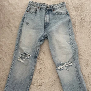 Ljusblå slitna jeans - Ljusblå jeans med snygga slitningar och hål på båda benen. Klassisk femficksmodell med raka ben och hög midja. Perfekta för en avslappnad och trendig look.