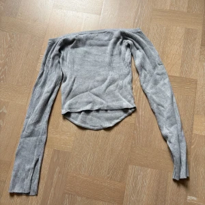 Grå ribbad offshoulder topp - Säljer en ljusgrå ribbad offshoulder topp från Garage i storlek M. Toppen har långa ärmar med slitsdetalj vid ärmsluten och är figurnära i modellen. 