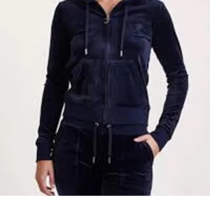 Mörkblå velour hoodie med dragkedja juciy  - Mysig mörkblå hoodie i mjuk velour med huva och snörning. Tröjan har dragkedja framtill, långa ärmar och kängurufickor. Perfekt för chill dagar eller när du vill vara extra bekväm.