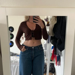 Brun croppad ribbad långärmad topp - Säljer en brun croppad topp med långa ärmar och snygg knytdetalj. Toppen har ribbad struktur och knyt framtill som gör att den kan användas både som den är och som en kofta .