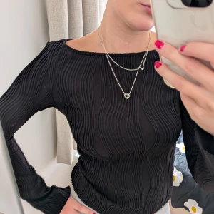 Svart ribbad långärmad topp - Säljer en svart långärmad topp med coola vågformade ribbade detaljer. Toppen har en tight passform och är tillverkad i ett stretchigt material som sitter snyggt på kroppen. Perfekt för dig som gillar stilrena men ändå unika plagg.