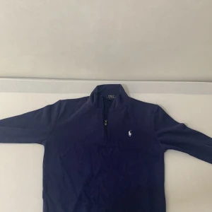 Marinblå half zip tröja Polo Ralph Lauren - Snygg marinblå långärmad tröja från Polo Ralph Lauren med half zip och klassisk broderad logga på bröstet. Tröjan är i mjuk bomull och har en stilren, normal passform. Perfekt för dig som gillar en clean och tidlös look.