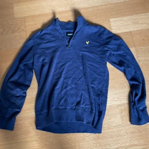 Marinblå half zip tröja Lyle & Scott - Säljer en marinblå långärmad tröja från Lyle & Scott med half zip och klassisk gul logga på bröstet. Tröjan har ribbade muddar och är perfekt för lager-på-lager. Skön och stilren att bära till jeans eller chinos. Stl 12-13 men ungefär som xs