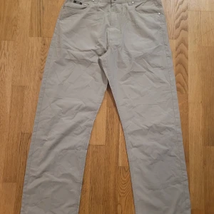 Beige chinos från Hugo Boss - Snygga beige chinos från Hugo Boss med klassisk femficksdesign och diskreta silverdetaljer. Byxorna har raka ben och normal passform, perfekt till en clean och stilren look. Tillverkade i mjuk bomull för skön känsla hela dagen.