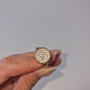 Guldfärgad ring med glittriga stenar - Snygg guldfärgad ring med rund topp täckt av små glittrande stenar. Ringen har en chunky känsla och ger ett lyxigt intryck.
