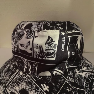 Svart och vit bucket hat med serietidningsmönster - Cool bucket hat från CD BLUES med svart och vitt serietidningsinspirerat mönster. Hatten har bred brätte och är tillverkad i bomull, perfekt för dig som vill sticka ut med en unik accessoar.