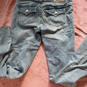 True Religion Becca Bootcut Jeans ljusblå - Ljusblå jeans från True Religion, modell Becca Mid Rise Bootcut. Klassisk femficksdesign med snygga detaljerade bakfickor och silverfärgade knappar. Jeansen har en bootcut-passform och är tillverkade i mjukt denimtyg för en avslappnad look. Köpt från johnells!!