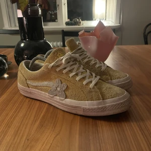 Golf Le Fleur Converse  - Unika Converse One Star Golf Le Fleur sneakers i gul mocka med vit blomdetalj på sidan och vita snören. Sulan har blommönster och skorna har en klassisk låg siluett. Perfekta för dig som vill sticka ut med en cool och färgglad look. Storlek 44, 800kr