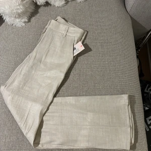 Beiga linnebyxor med utsvängda ben Nelly - Snygga beiga linnebyxor från Nelly i modell med låg midja och utsvängda ben. Byxorna har bälteshällor och är tillverkade i ett lätt och luftigt linnematerial, perfekta för en chill och stilren look. Något uppsydda, passar för 1,58cm långa och kortare. 