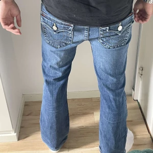 True Religion blå bootcut jeans 32 - Säljer ett par ikoniska True Religion jeans i klassisk blå tvätt med snygga kontrastsömmar och stora fickor med vita knappar bak. Modellen har bootcut-ben och låg midja, tillverkade i slitstarkt jeanstyg. Helt nya, tveka inte om att skriva om ni har frågor. 🙌