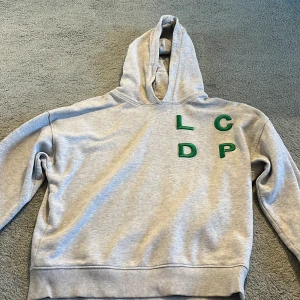 Grå hoodie från Les Coyotes de Paris - ÄKTA!! Snygg ljusgrå hoodie från Les Coyotes de Paris med gröna bokstäver 'LCDP' på bröstet. Tröjan har huva!