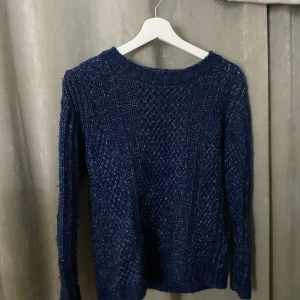 Mörkblå stickad tröja med struktur - Mysig mörkblå stickad tröja med snyggt strukturerat mönster och rund halsringning. Tröjan har långa ärmar och ribbade muddar vid ärmslut och nederkant. Perfekt för lager-på-lager och chill dagar. Storleken är M men passar som S
