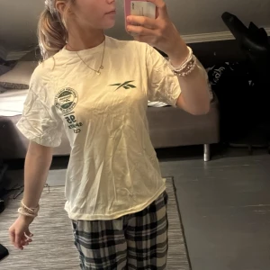 Vit Reebok t-shirt - Vit t-shirt från Reebok med grönt tryck på bröstet och vänster sida. Klassisk rund hals och korta ärmar, perfekt för en chill och sportig look. Skön passform i mjuk bomull, enkel att matcha med jeans eller mjukisbyxor.