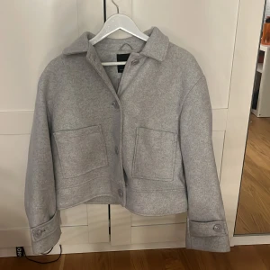 Grå overshirt från 157, storlek M - Snygg grå overshirt från 157 i storlek M. Jackan har en boxig passform, stora fickor framtill, klassisk krage och knäppning med knappar. Perfekt att slänga över en hoodie eller t-shirt för en chill look.