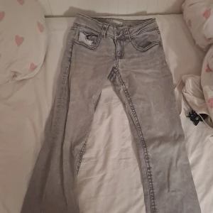 Grå bootcut jeans med låg midja - Säljer ett par ljusgrå jeans med bootcut och låg midja. Jeansen har klassiska fem fickor, snygga detaljer på bakfickorna och är i stretchigt jeanstyg. Perfekta för dig som gillar en avslappnad men ändå trendig look.