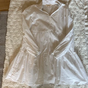 Vit kortklänning Pernilla Wahlgren  - Superfin vit kortklänning från Pernilla Wahlgren med lång ärm och lätt vidd i kjolen. Klänningen har en avslappnad passform, liten krage och rynkade detaljer framtill💗