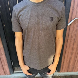 Brun t-shirt från Burberry - Snygg brun t-shirt från Burberry med diskret logga på bröstet. Klassisk rund halsringning och korta ärmar. Tillverkad i mjuk bomull som känns skön mot huden. Perfekt för dig som gillar stilrena och exklusiva plagg.