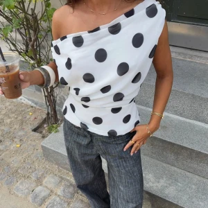Prickig oneshoulder topp med snörning - Snygg vit offshoulder topp från DesignBySi med svarta prickar och draperad passform. Toppen har snörning i ryggen för en justerbar look. Oanvänd, köpt förra månaden och storlek M/L 🥰