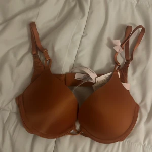 2 cups bra Victoria's Secret - Snygg brun bh från Victoria's Secret med släta kupor och justerbara axelband. Bh:n har en enkel design med små rosetter på banden och stängs med hyskor bak. Materialet är mjukt och följsamt, perfekt för en bekväm känsla hela dagen.