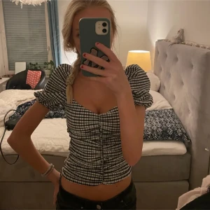 Svartvit rutig blus med puffärm - Supersöt blus i svartvitt rutigt mönster med puffiga korta ärmar och söt hjärtformad urringning. Smickrande rynkdetalj framtill och figurnära passform. Perfekt att styla med jeans eller kjol för en trendig look. Från bikbok. Inte mina bilder!! Är i storlek M och i bilden är tröjan storlek xs 